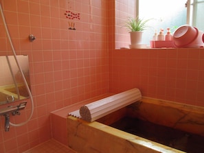 A bathroom with pink tiles, a bathtub with a marble surround, a sink with a mirror, and a window with a plant and toiletries on the windowsill. - Pension Rapan (Katashina)
