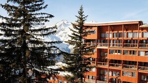 A multi-story building with balconies, surrounded by snow-covered mountains and evergreen trees.