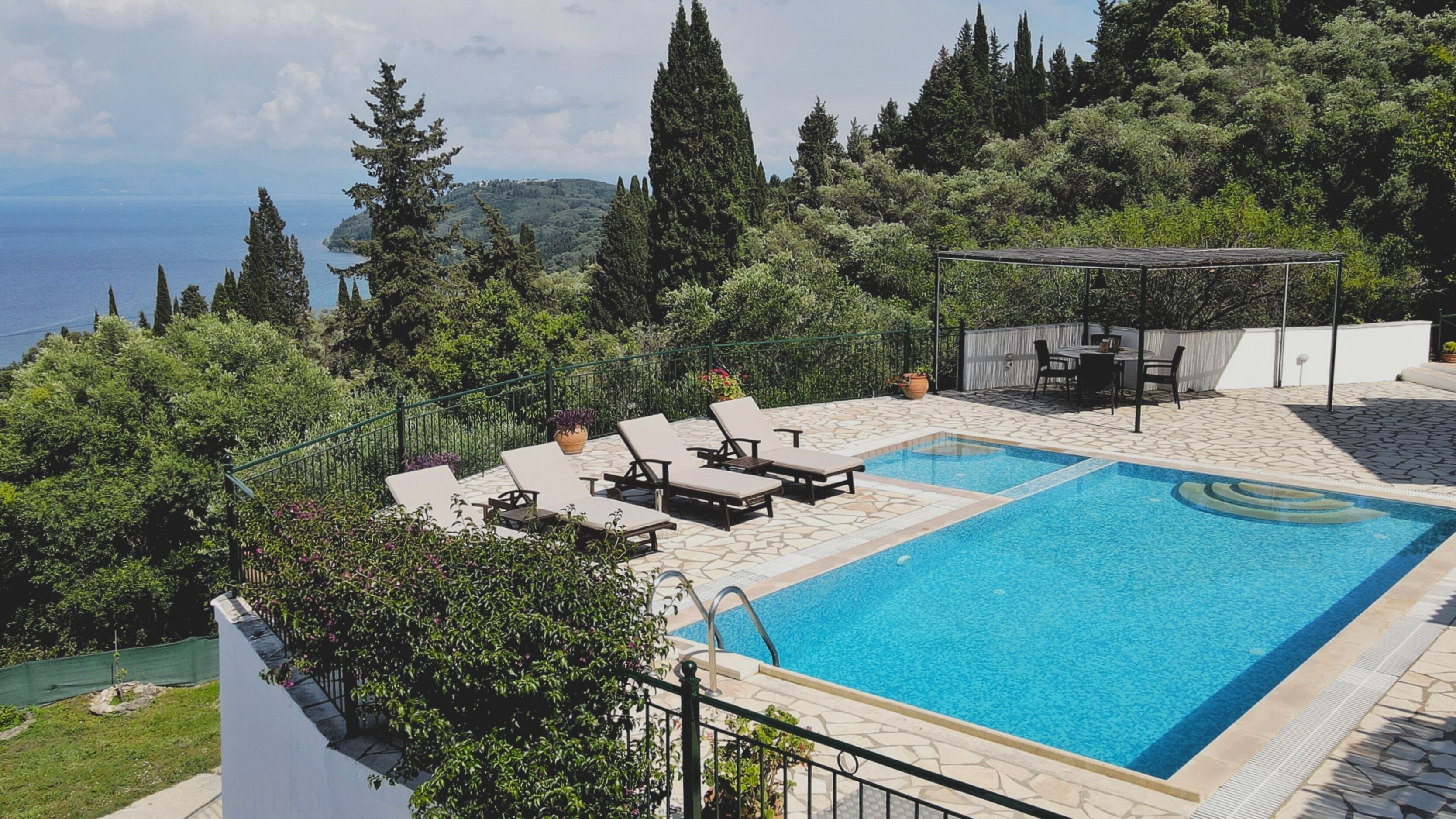 Une piscine dotée de chaises longues et d’une pergola, entourée d’une végétation luxuriante et offrant une vue imprenable sur un paysage magnifique.