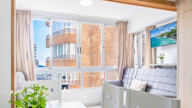 A modern room with a large window, a sofa, a TV, and a potted plant. - Inlesa 4-B Apartment Levante Beach (Benidorm)