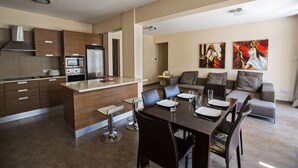 Eine moderne Küche mit Kochinsel, Essbereich mit Tisch und Stühlen sowie ein Wohnbereich mit Sofa und Kunstwerken.