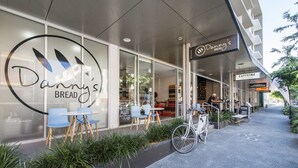 A storefront with a large sign reading "Danny's Bread" and a bicycle parked outside. - Doubleone3 Apartments (Teneriffe)