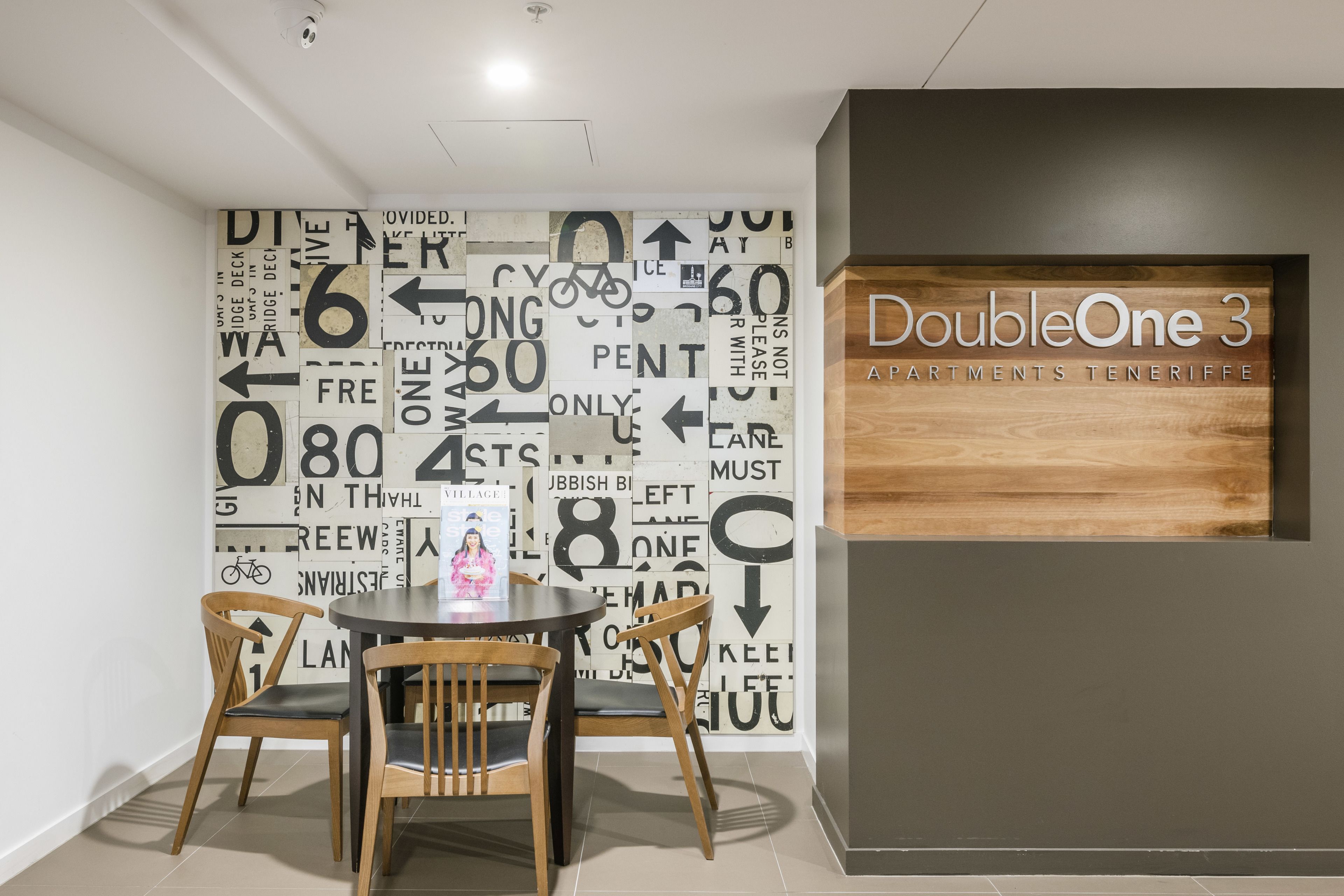 A dining area with a table and chairs, a wall with directional signs, and a sign for "DoubleOne 3 Apartments Tenerife".