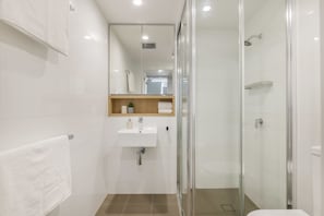 A modern bathroom with a glass shower enclosure, a wooden vanity, and a white sink. - Doubleone3 Apartments (Teneriffe)