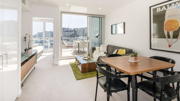 A modern living room with a dining area, a sofa, a coffee table, and a view of the city through large windows. - Doubleone3 Apartments (Teneriffe)