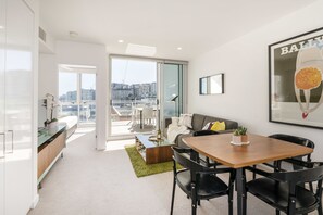 A modern living room with a dining area, a sofa, a coffee table, and a view of the city through large windows. - Doubleone3 Apartments (Teneriffe)