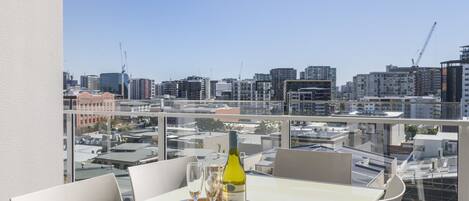 A table with a bottle of wine and glasses on a tray, overlooking a cityscape with buildings and cranes.