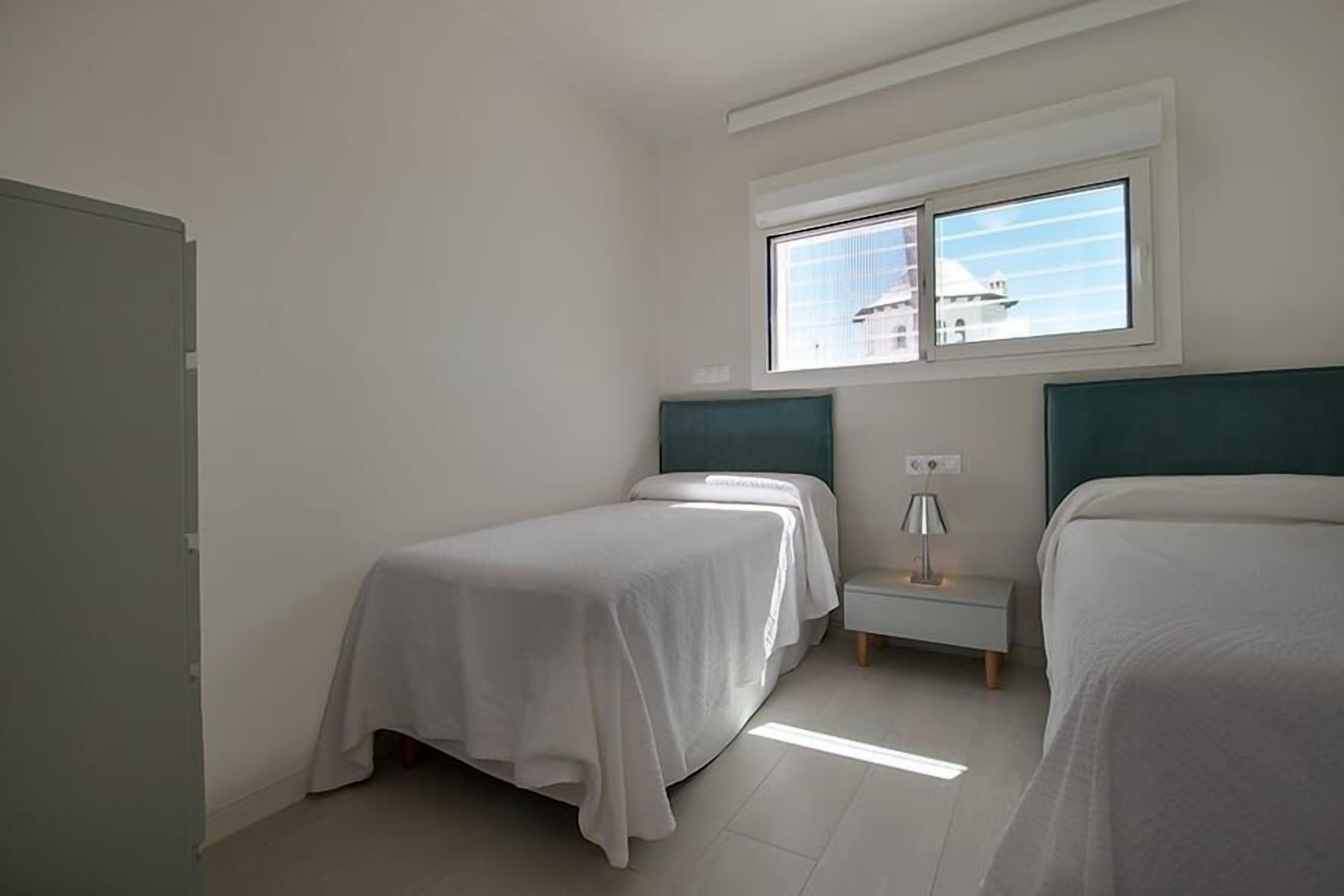 A bedroom with two beds, a window, a nightstand, and a lamp.