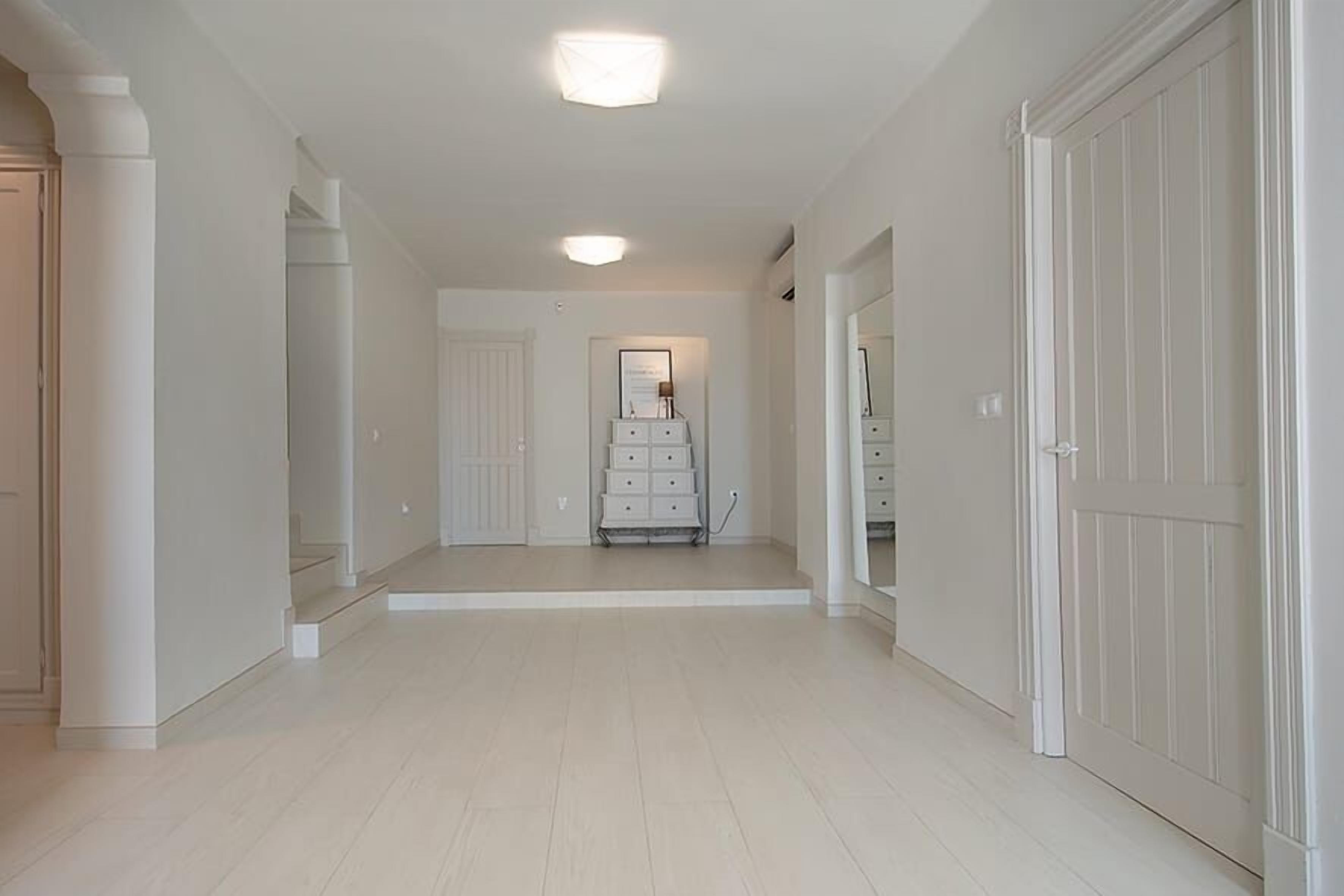 A hallway with white walls and doors, a light fixture on the ceiling, and a small white dresser against the wall.