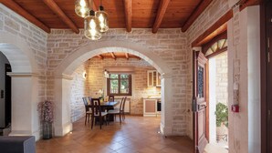 A spacious dining area with a stone wall, wooden ceiling beams, and a view into the kitchen. - Family villa Elia with heated pool, 2 minutes walking to local amenities (Rethymno)