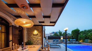 An outdoor dining area with a pool, wooden furniture, and a stone wall. - Family villa Elia with heated pool, 2 minutes walking to local amenities (Rethymno)