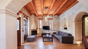 A living room with a fireplace, a sofa, a coffee table, and a TV. - Family villa Elia with heated pool, 2 minutes walking to local amenities (Rethymno)