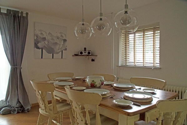 A dining room with a wooden table set for six, surrounded by six chairs. There are three hanging pendant lights above the table.