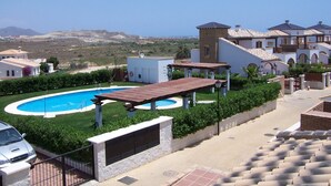 A pool area with a pergola, a white building with a tower, and a view of distant hills. - VILLA ALANDALUS VERA PLAYA (Vera playa)