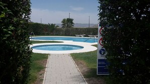 A swimming pool with a paved walkway leading to it, surrounded by greenery and a sign indicating a hospital nearby. - VILLA ALANDALUS VERA PLAYA (Vera playa)