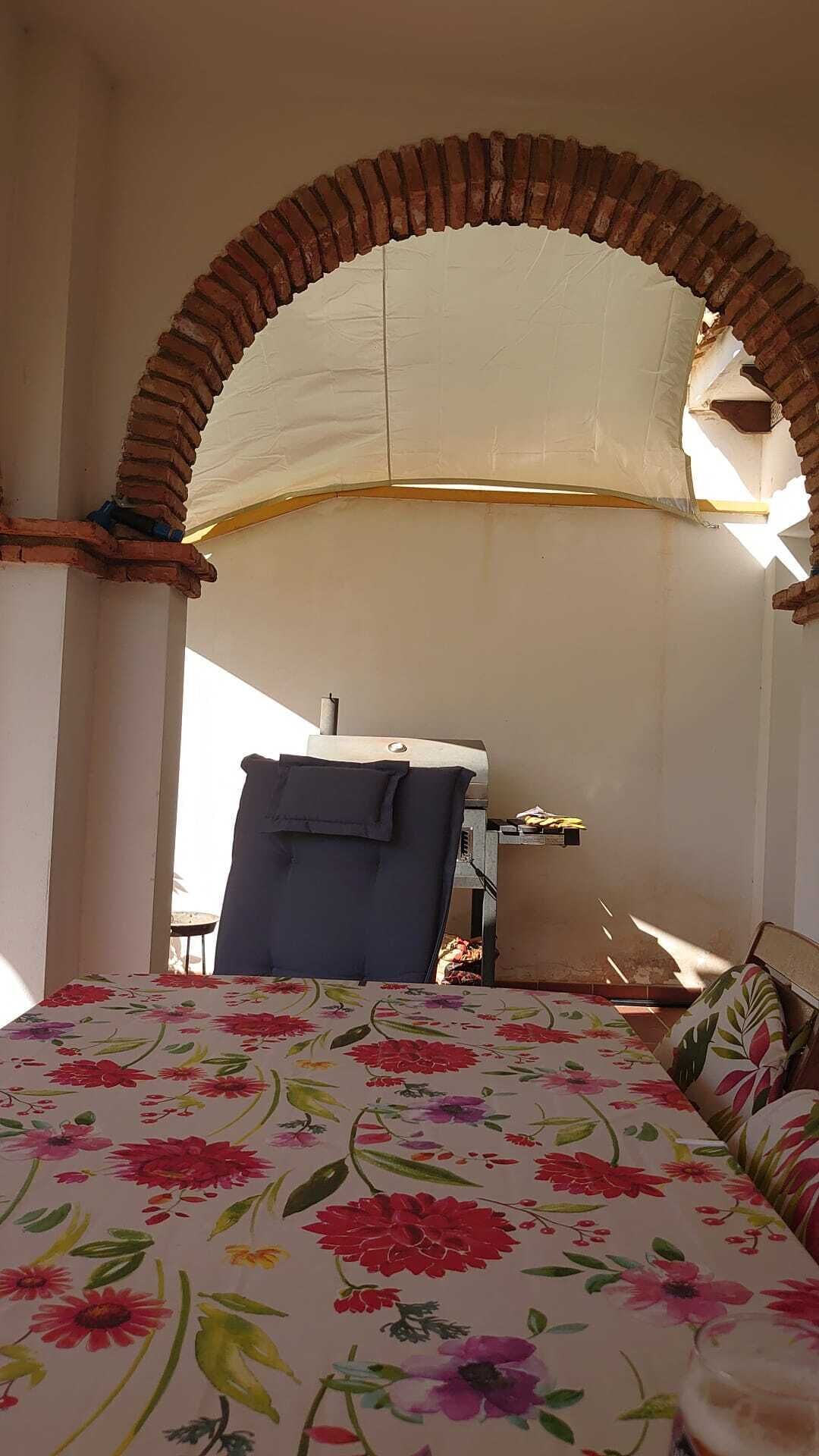 Une pièce avec un lit placé sous une arche en briques, une chaise et une table recouverte d’une nappe blanche.