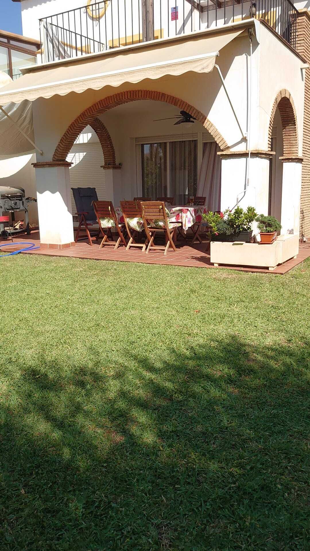 Un espace extérieur abrité, aménagé avec une table et des chaises, un ventilateur de plafond et des plantes en pot.