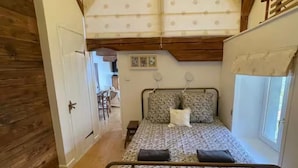 Une chambre à coucher avec un lit, des poutres en bois, une fenêtre et une porte.