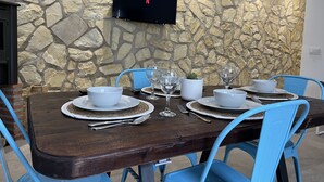 A dining area with a stone wall, a flat-screen TV mounted above the table, and blue chairs.