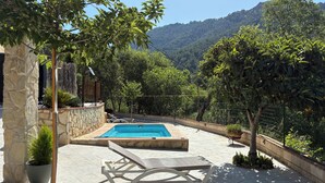 A pool area with a stone wall, lounge chairs, and potted plants.