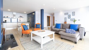 A modern living room with a grey sofa, orange chairs, a white coffee table, and a kitchen in the background. - Apartment Goncalves,  (Arco da Calheta)