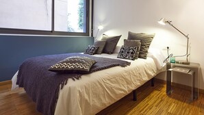 A bedroom with a bed, pillows, a bedside table with a lamp, and a window.