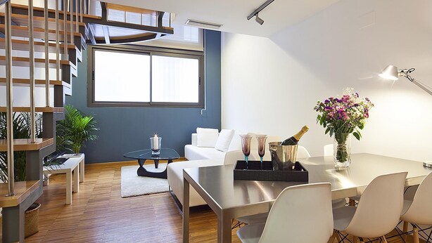 A modern living space with a dining area, a staircase, and a large window providing natural light.
