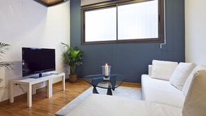 A modern living room with a flat-screen TV, a white sofa, a glass coffee table, and a potted plant.