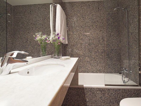 A modern bathroom with a granite backsplash, a white sink, a mirror, and a glass-enclosed shower.