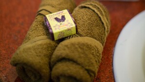 Une serviette sur laquelle repose un petit objet violet et jaune, un verre d’eau et un bouquet de fleurs sur un comptoir.