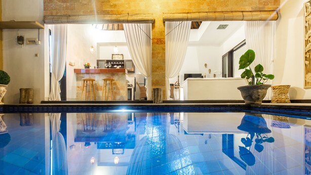 Une piscine dont l’eau est si claire qu’elle reflète parfaitement l’environnement, un coin bar avec des tabourets et une plante en pot.