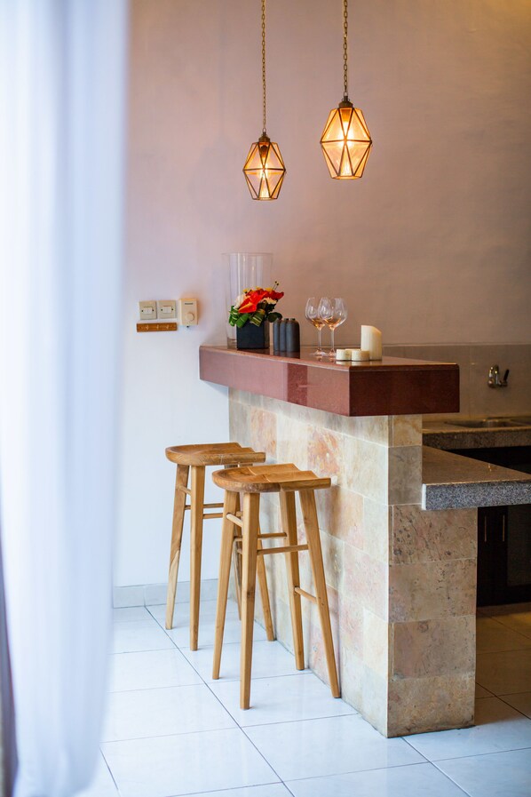 A kitchen with a marble island, wooden stools, pendant lights, and a countertop with glasses and candles. - Villa Leon (Seminyak)