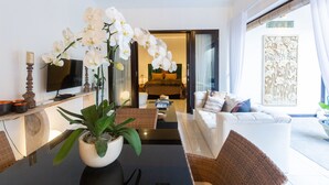 Un salon moderne avec un coin repas, comprenant une grande orchidée en pot, un téléviseur à écran plat, un canapé et une table basse.