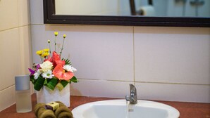 Une salle de bain avec un lavabo blanc, un miroir et un vase de fleurs posé sur le comptoir.
