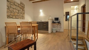 A cozy kitchen with a stone wall, wooden ceiling beams, and a dining area with wicker chairs and a wooden table. - Il Cortile Apartment in Rovinj centre (Rovinj)