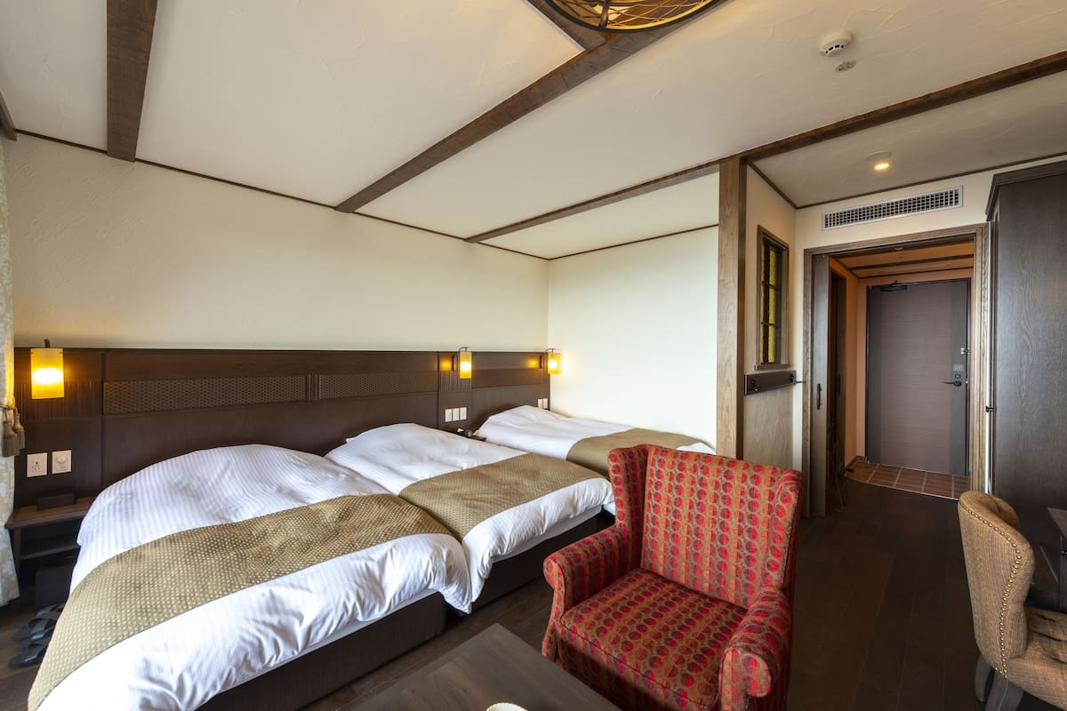 Een hotelkamer met een groot bed, een rode fauteuil met patroon en een houten plafond.