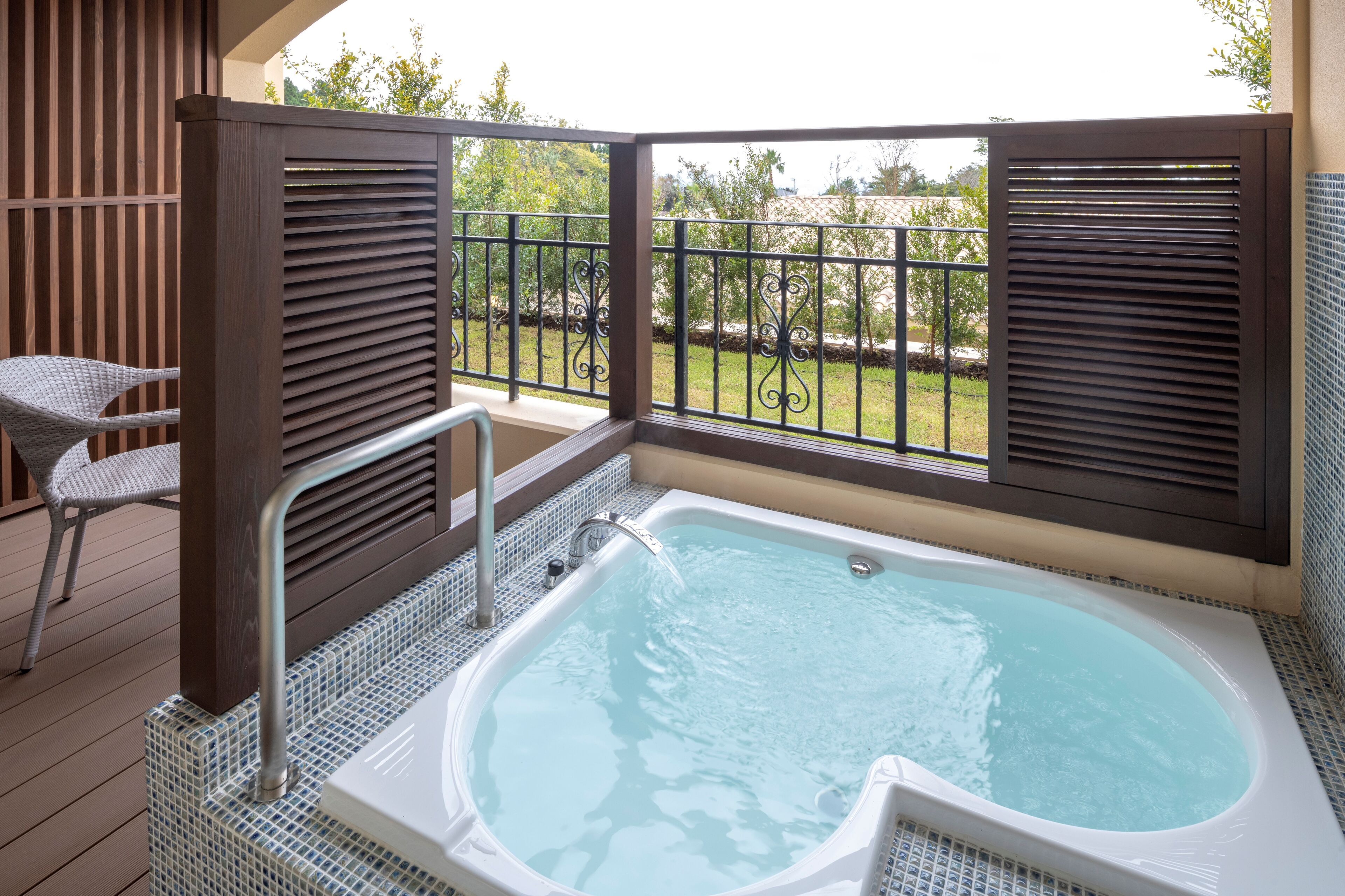A spa area with a hot tub, a chair, and a view of a garden.