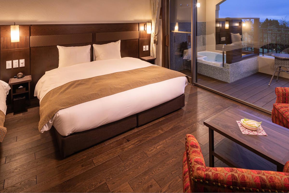 Een hotelkamer met een groot bed, een balkon met een hottub en twee fauteuils.