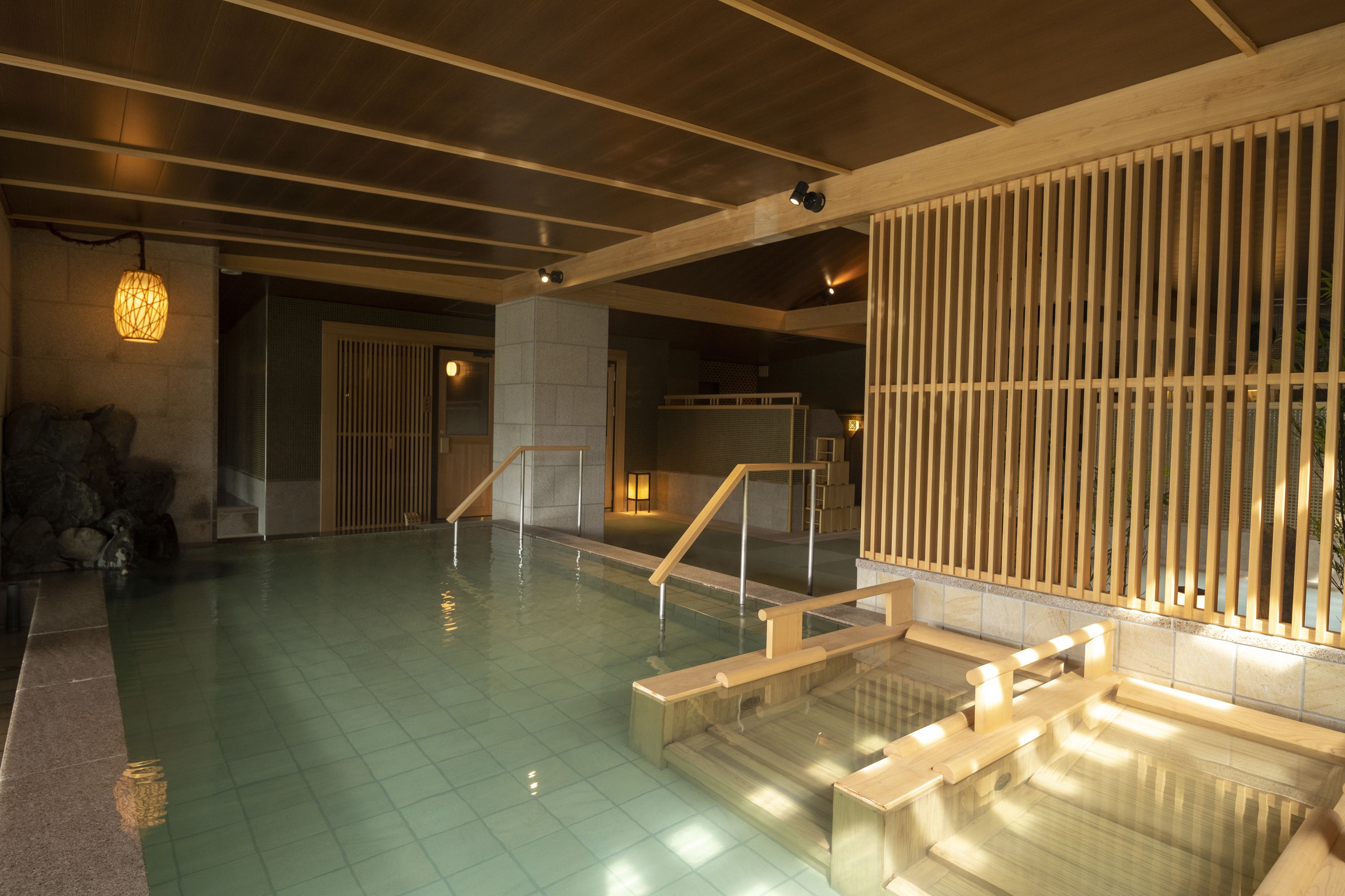 A spacious indoor swimming pool with clear water, wooden steps, and a tiled floor.