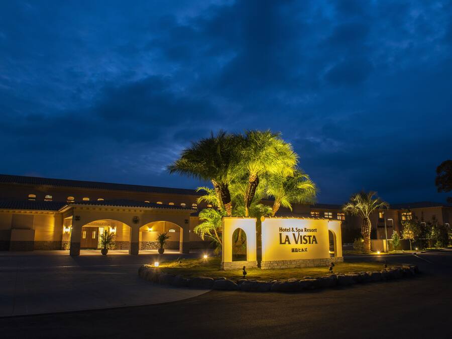 A hotel entrance with a sign reading "Hotel & Spa Resort LA VISTA" and a palm tree in the foreground.