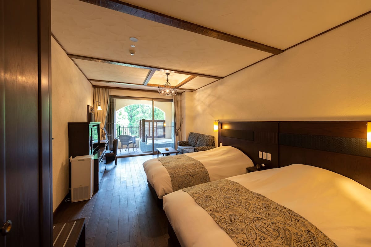 Een hotelkamer met twee bedden, een bureau, een stoel en uitzicht op het omliggende landschap.