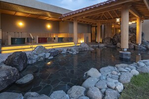 Un edificio de estilo japonés tradicional con un estanque de piedra, vigas de madera y una zona de estar cubierta.