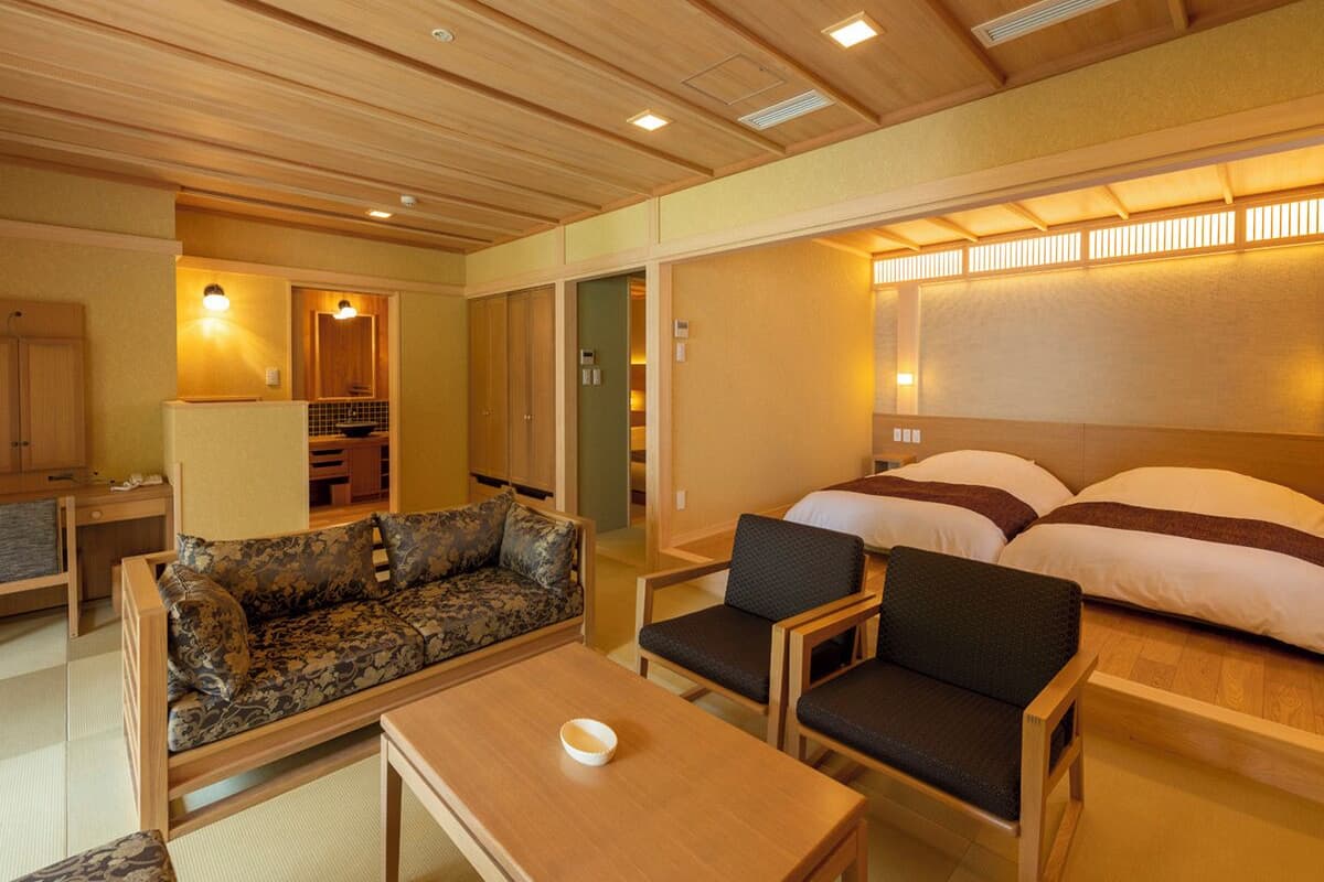 Een traditionele Japanse kamer met tatami vloeren, een laag houten plafond, een futonbed, een kleine eettafel en een bank.