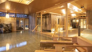 A spacious indoor area with wooden flooring, a central seating area with a glass barrier, and a stone wall with a water feature. - LA VISTA Kirishima Hills (Kirishima)