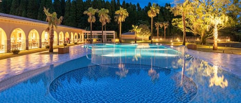 Zona de piscina con suelo de baldosas y un edificio con ventanas de arco al fondo.