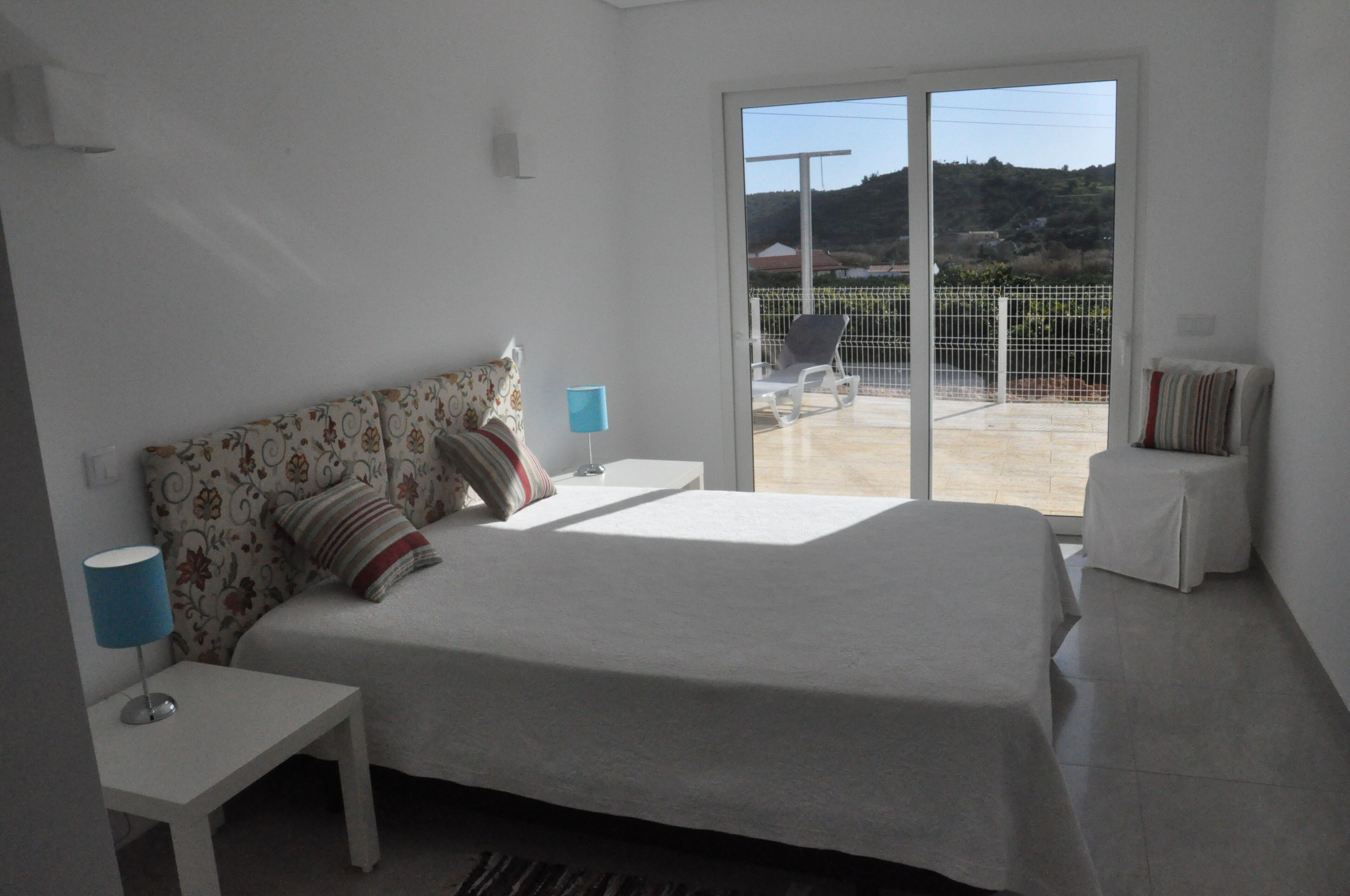 Una camera da letto con un letto, un comodino, una lampada e vista sul balcone.