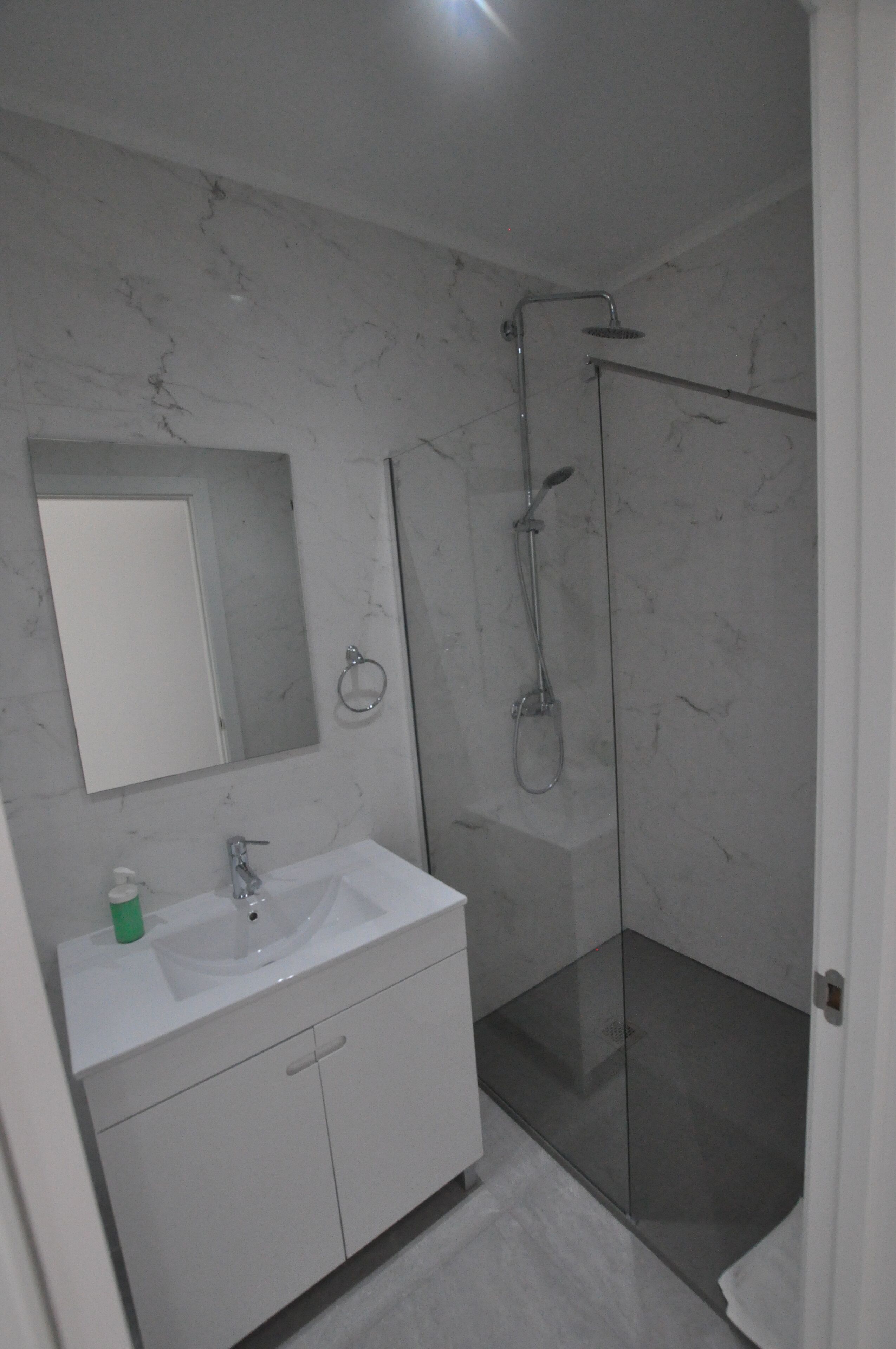 A bathroom with a marble wall, a glass shower enclosure, and a white vanity with a mirror.
