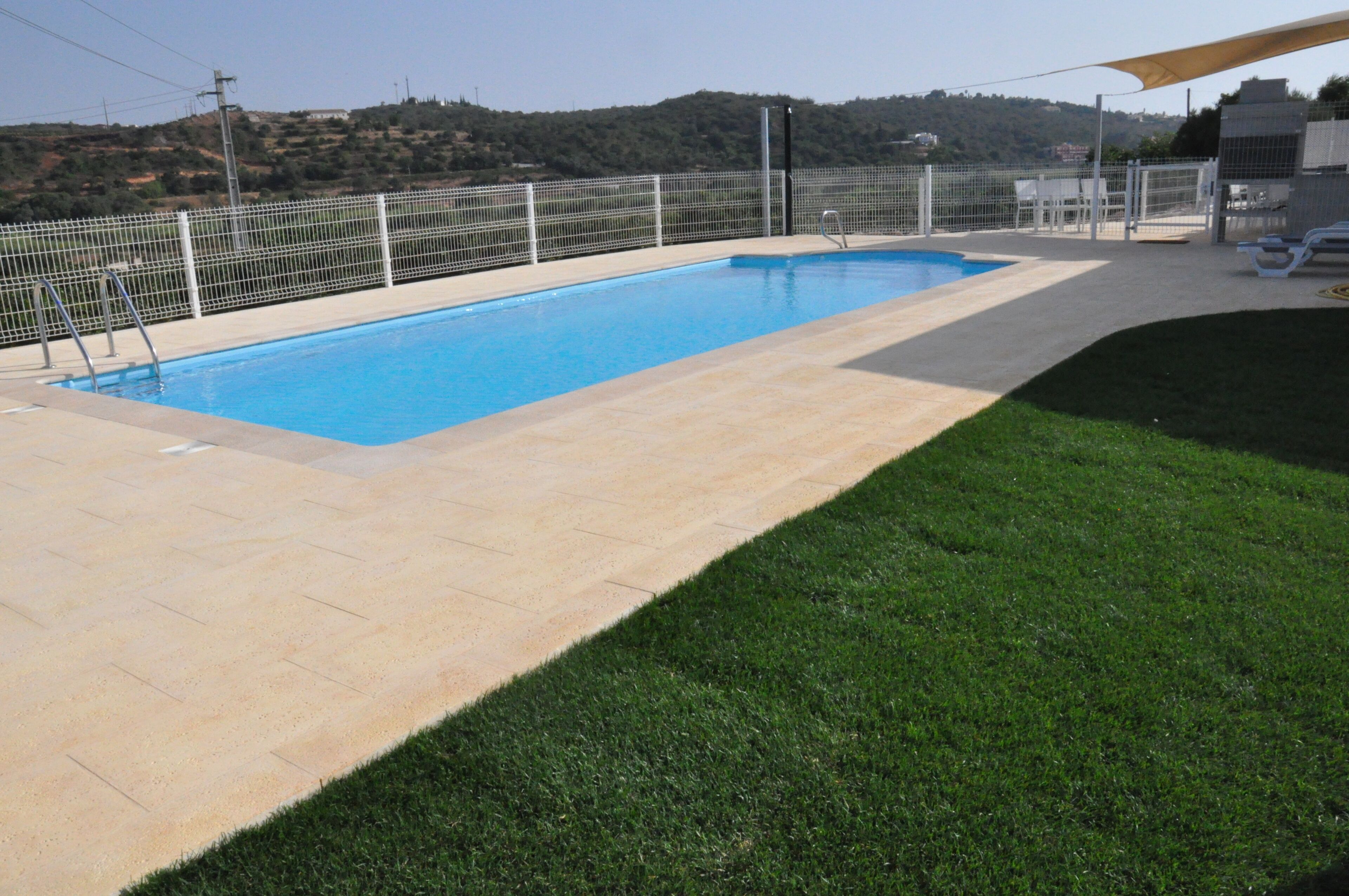Una piscina rectangular con cerca blanca y zona de césped.