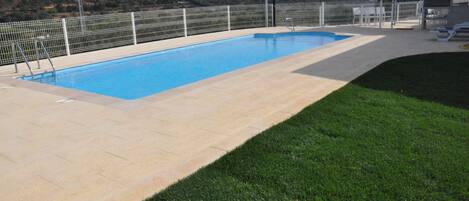 Una piscina rectangular con cerca blanca y zona de césped.
