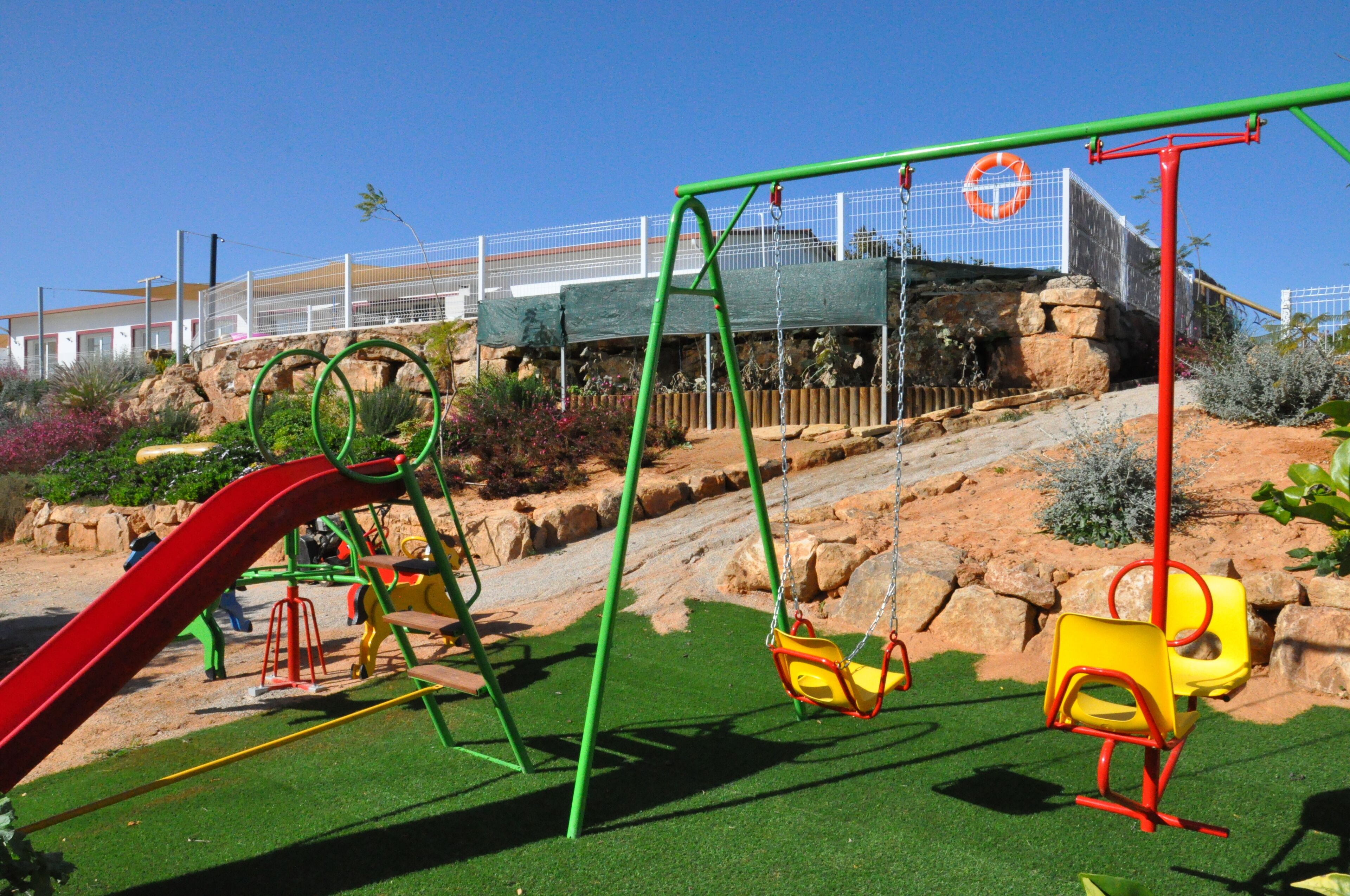 A playground with swings and slides, surrounded by rocks and plants.